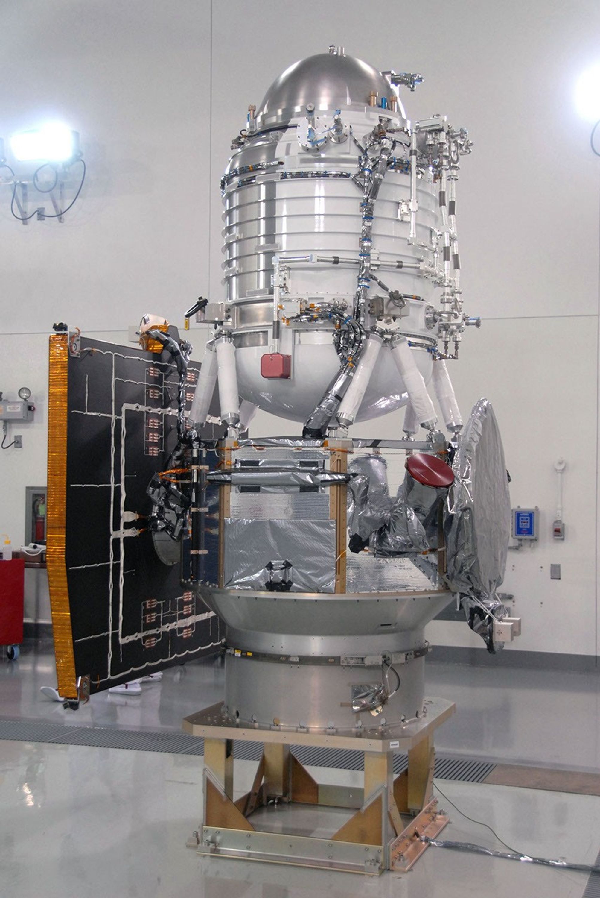 NASA's Wide-field Infrared Survey Explorer spacecraft is situated on a work stand. At left on the spacecraft is the fixed panel solar array. In front, the square is the HGA Slotted Array (Ku-Band).