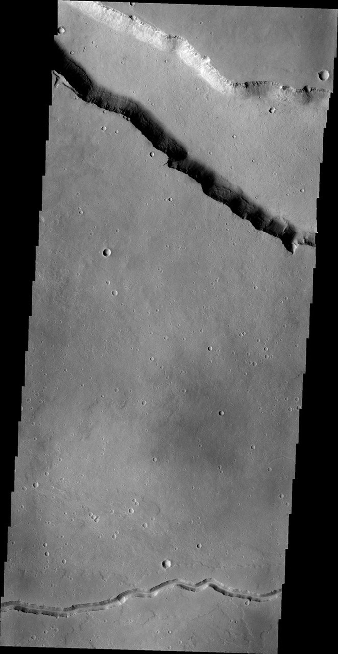 This NASA 2001 Mars Odyssey spacecraft image shows two different types of linear depressions. The wide depression at the top of the frame is Elysium Fossae, which most likely formed due to tectonic activity.