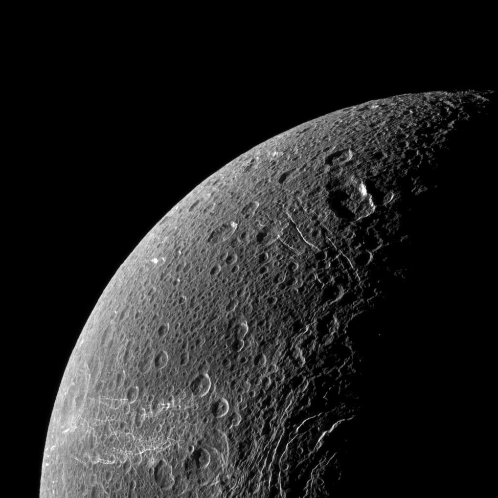 Wispy terrain reflects sunlight brightly in the lower left of this NASA Cassini image of the northern latitudes of Saturn's moon Dione.