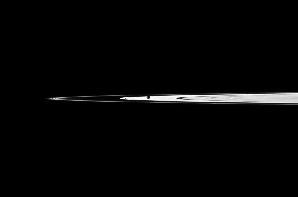 NASA's Cassini spacecraft looks past the cratered south polar area of Saturn's moon Rhea to spy the moon Dione and the planet's rings in the distance. Dione's 'wispy' terrain can be seen on the trailing hemisphere of that moon.
