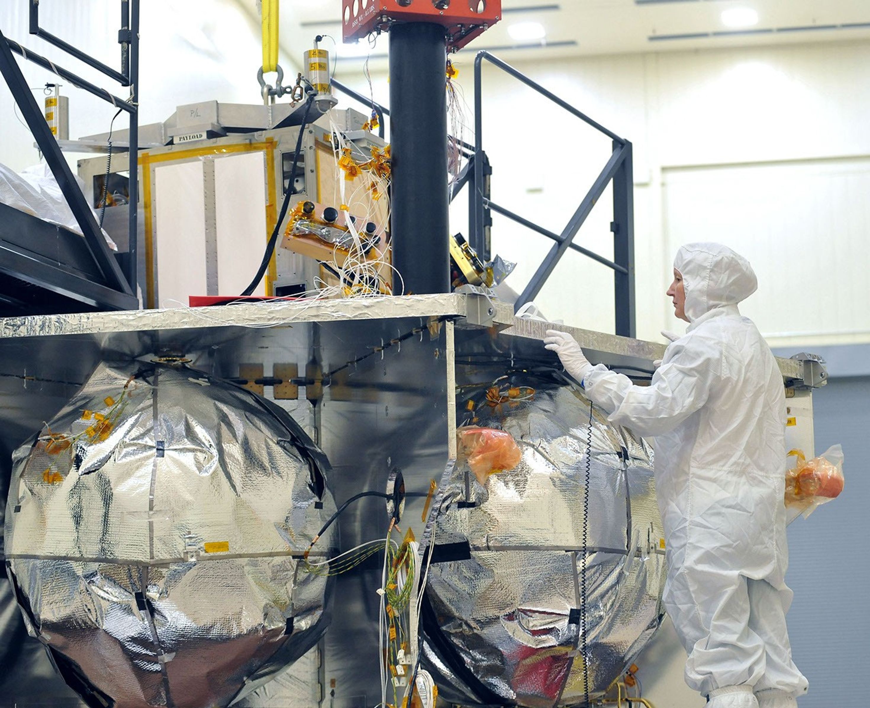 A technician inspects the special radiation vault being installed atop the propulsion module of NASA's Juno spacecraft; the vault has titanium walls to protect the spacecraft's electronic brain and heart from Jupiter's harsh radiation environment.