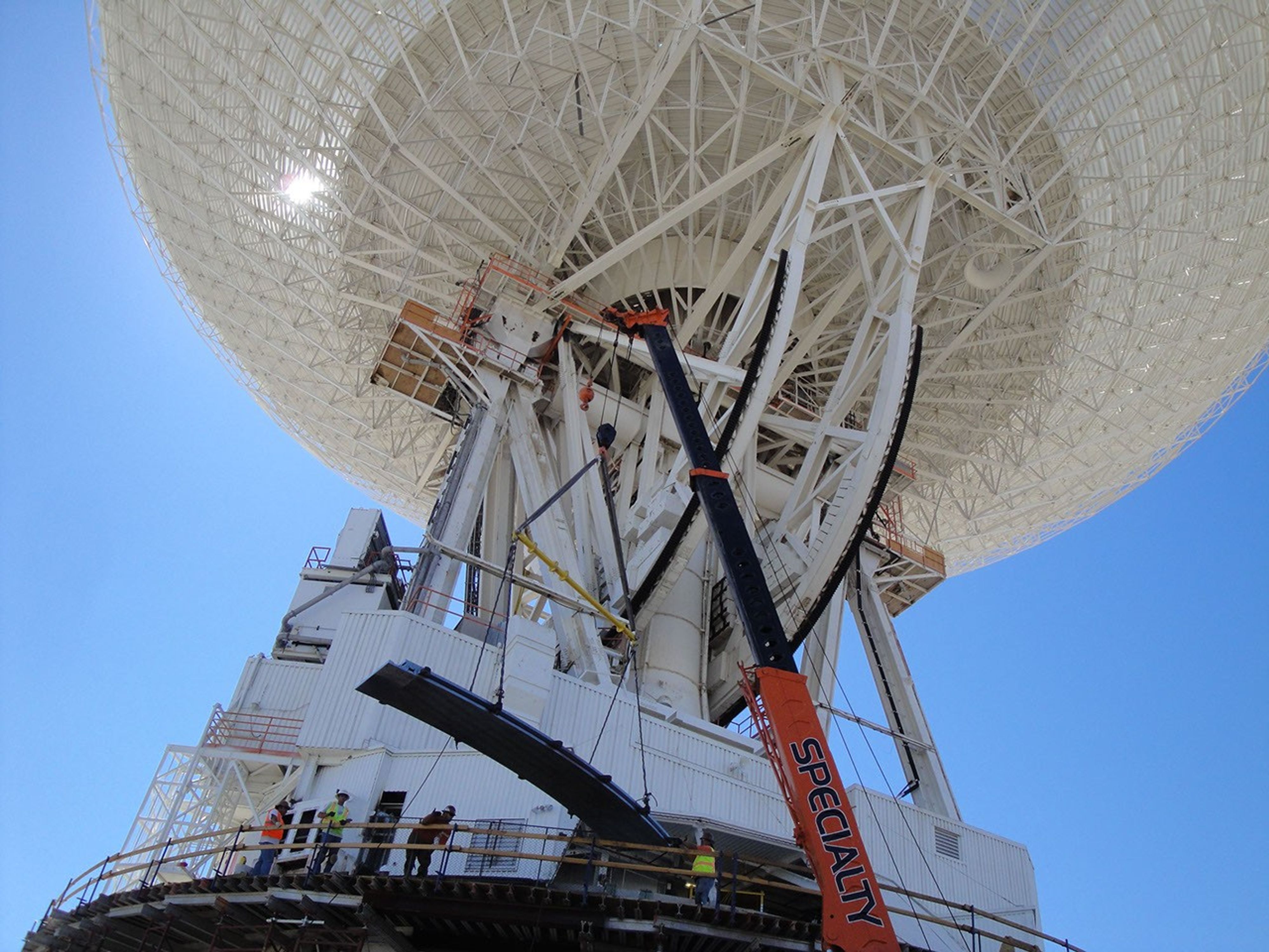 Under the unflinching summer sun, workers at NASA's Deep Space Network complex in Goldstone, Calif., use a crane to lift a runner segment that is part of major surgery on a giant, 70-meter-wide antenna.
