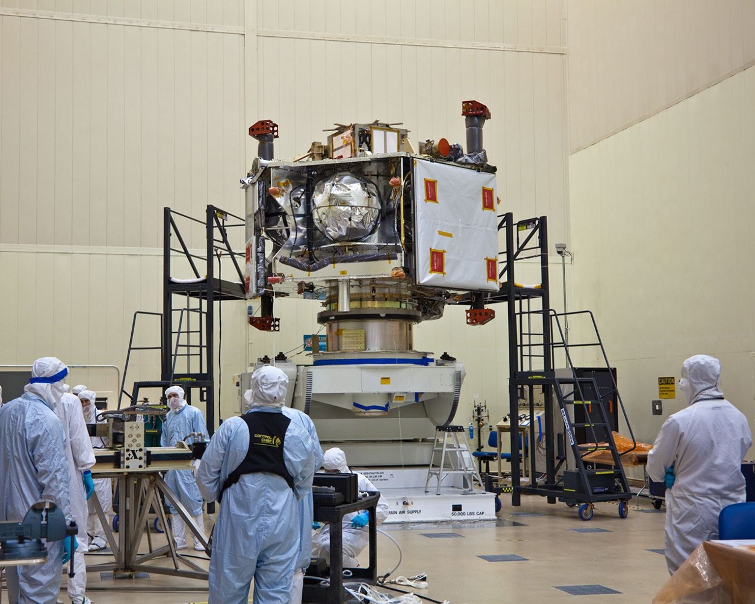 NASA's Juno spacecraft rests atop its rotation fixture awaiting transfer to a shipping crate prior to environmental testing; the large white square on the spacecraft's right is largest of six microwave radiometer antennas, masked by protective covering.