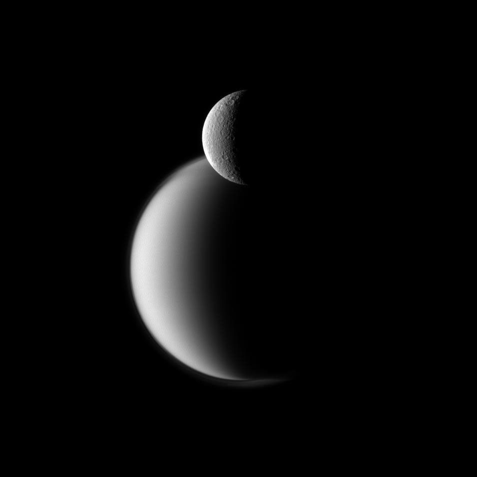 Craters appear well defined on icy Rhea in front of the hazy orb of the much larger moon Titan in this view from NASA's Cassini spacecraft.