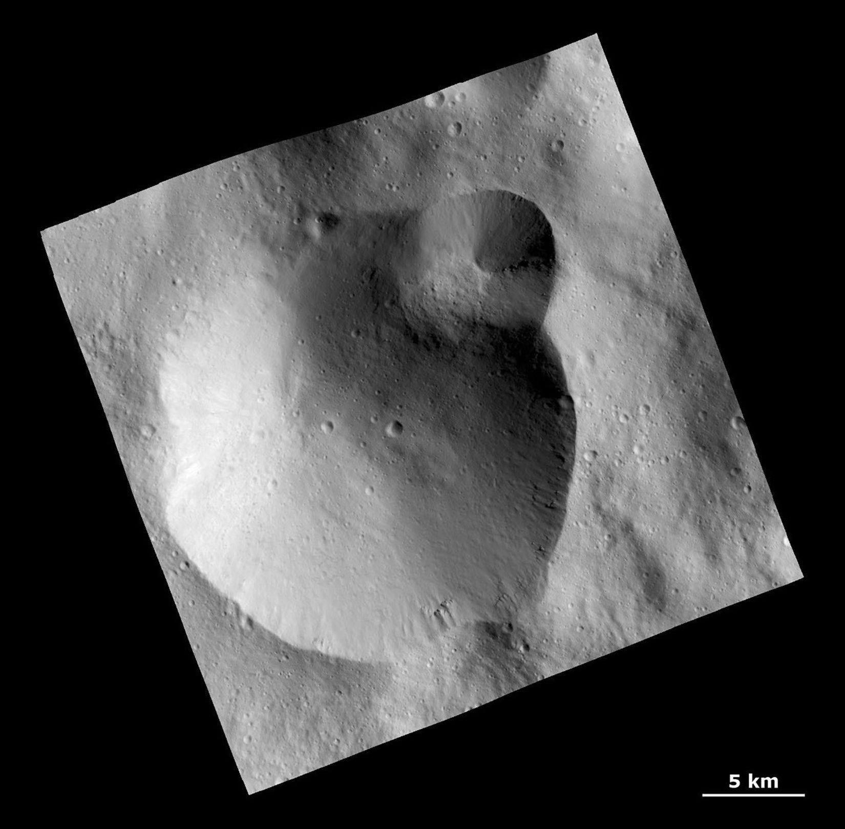 This image from NASA's Dawn spacecraft shows a large crater with several smaller craters at the edge on the giant asteroid Vesta. Rough texture in the crater wall at far right may be the underlying bedrock.