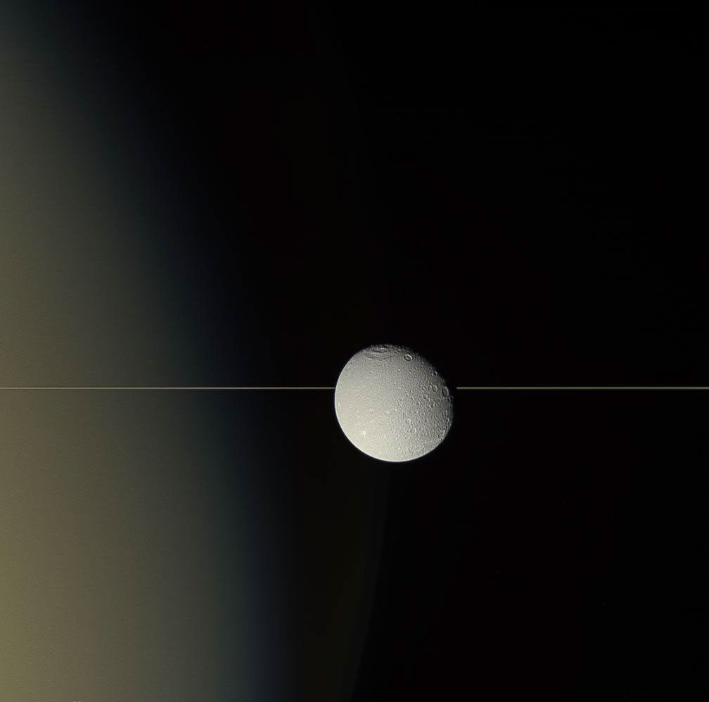 Saturn's moon Dione drifts before the planet's rings, seen here by NASA's Cassini spacecraft almost edge on. For all their immense width, the rings are relatively paper-thin.