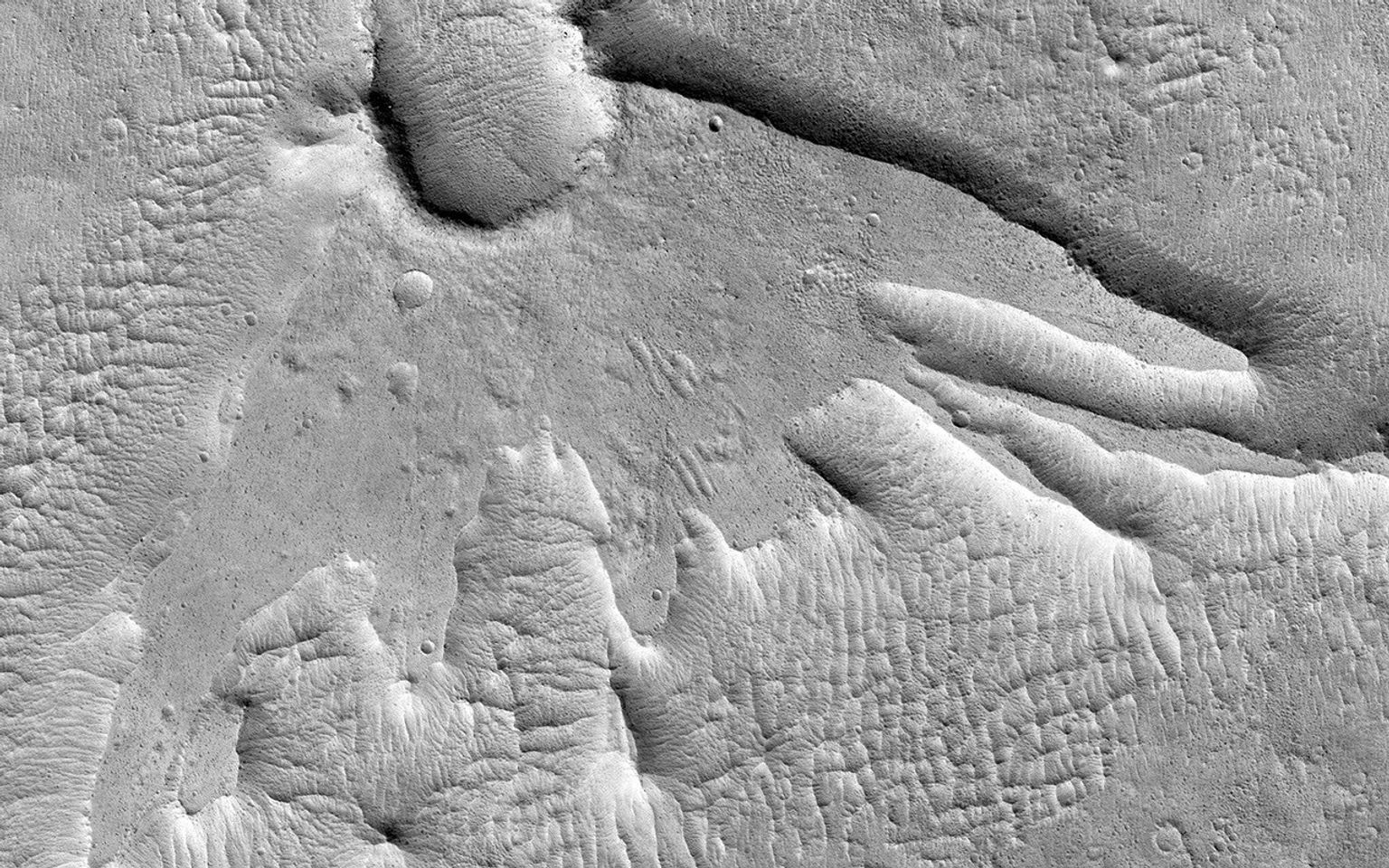 This non-circular pit seen in this image from NASA's Mars Reconnaissance Orbiter is due to a low angle impact from an asteroid or comet. The raised plateau west of the crater was where most of the impact debris landed.