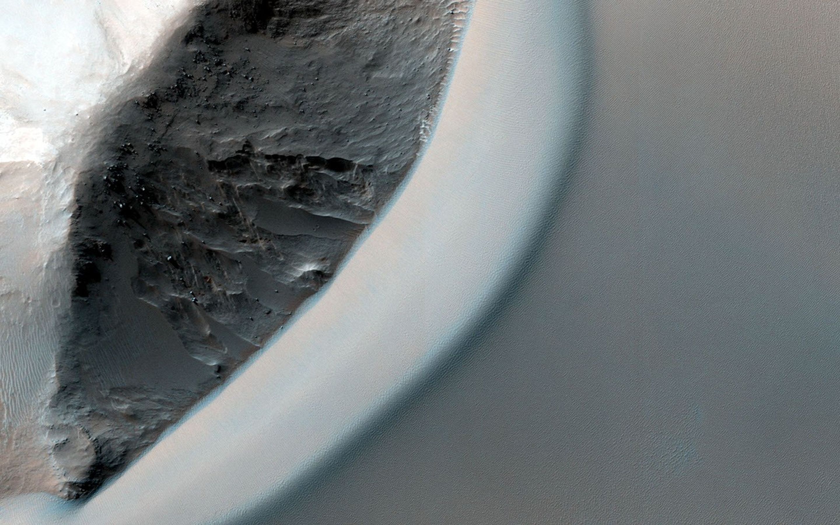 This dramatic image observed by NASA's Mars Reconnaissance Orbiter shows dark rippled bodies of sand, sometimes in the form of dunes, streaming through Ganges Chasma. The floor of the canyon is covered by hills and mesas.