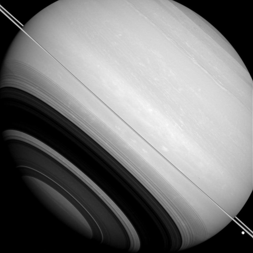NASA's Cassini orbiter shows Saturn is circled by its rings (nearly edge-on in this image), as well as by the moons Tethys (the large bright body near the lower right corner) and Mimas (seen as a slight crescent against Saturn's disk above the rings).
