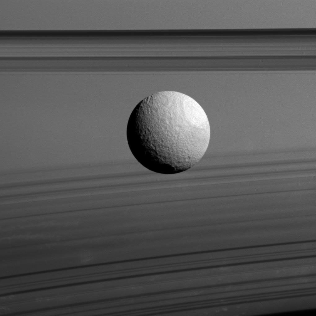 Saturn's moon Tethys appears to float between two sets of rings in this view from NASA's Cassini spacecraft, but it's just a trick of geometry. The rings, which are seen nearly edge-on, are the dark bands above Tethys.