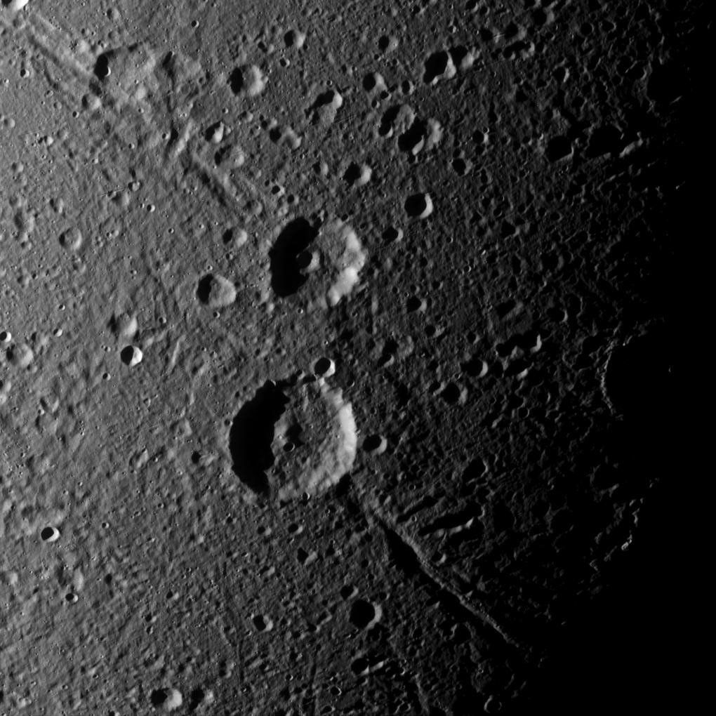 Cassini captures a crater duo (Italus on ancient trough called Petelia Fossae, and Caieta, atop Helorus Fossa) on Saturn's moon Dione that is superimposed on older, linear features.
