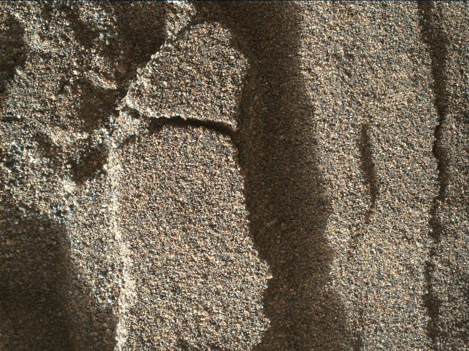 This view shows grains of sand where NASA's Curiosity Mars rover was driven into a shallow sand sheet near a large dune. The disturbance by the wheel exposed interior material of the sand body, including finer sand grains than on the undisturbed surface.