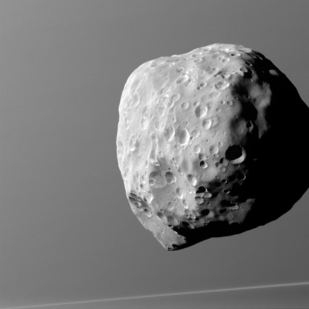 Epimetheus, seen here by NASA's Cassini spacecraft, with Saturn in the background, is lumpy and misshapen, thanks in part to its size and formation process. Bombardment over the eons has left this tiny moon's surface heavily pitted.