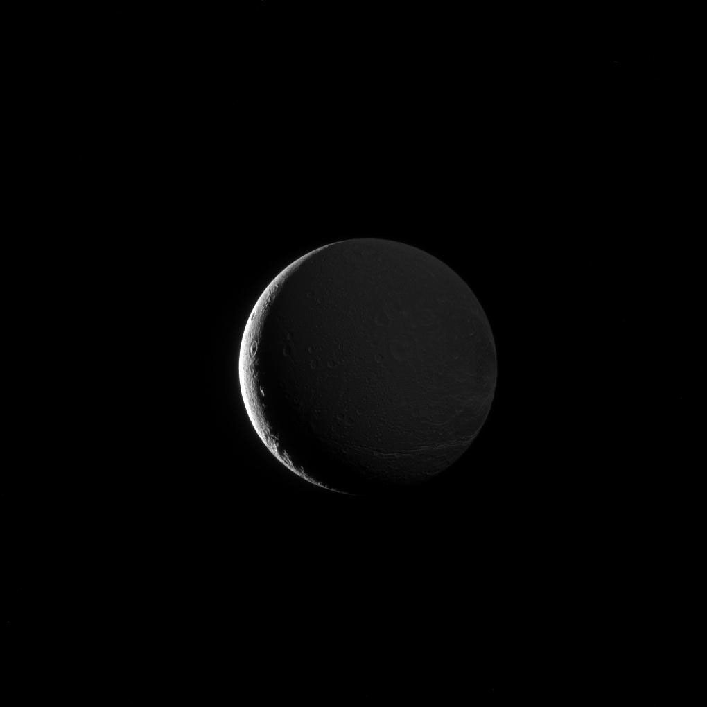 Dione's lit hemisphere faces away from NASA's Cassini spacecraft's camera, yet the moon's darkened surface features are dimly illuminated in this image, due to Saturnshine.