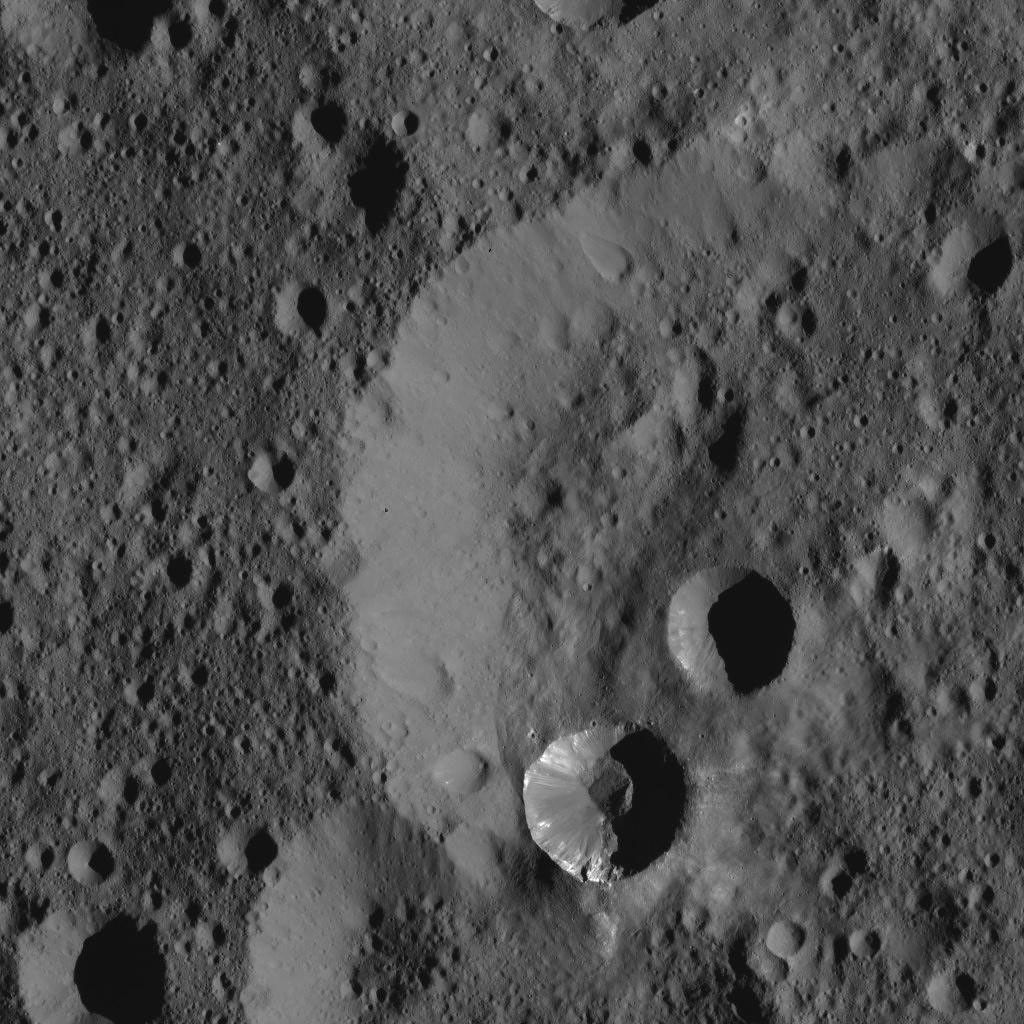 This view from NASA's Dawn spacecraft shows two relatively young craters superimposed on a larger, older impact feature. The smaller craters have streaks of bright material on their walls.
