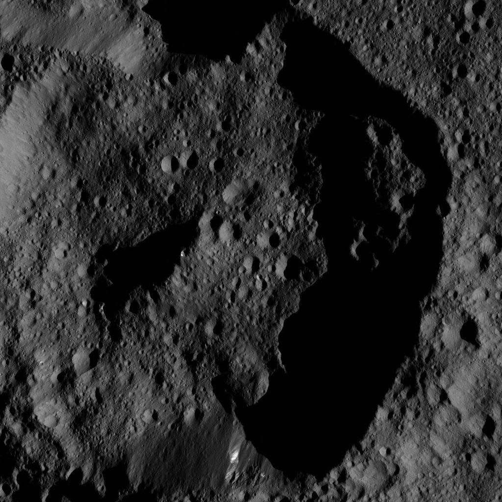 This image. taken on June 12, 2016, from NASA's Dawn spacecraft shows dimly lit, cratered terrain on Ceres. Bright streaks of material are visible on one section of the crater wall (at bottom), and near the top of its central peak.
