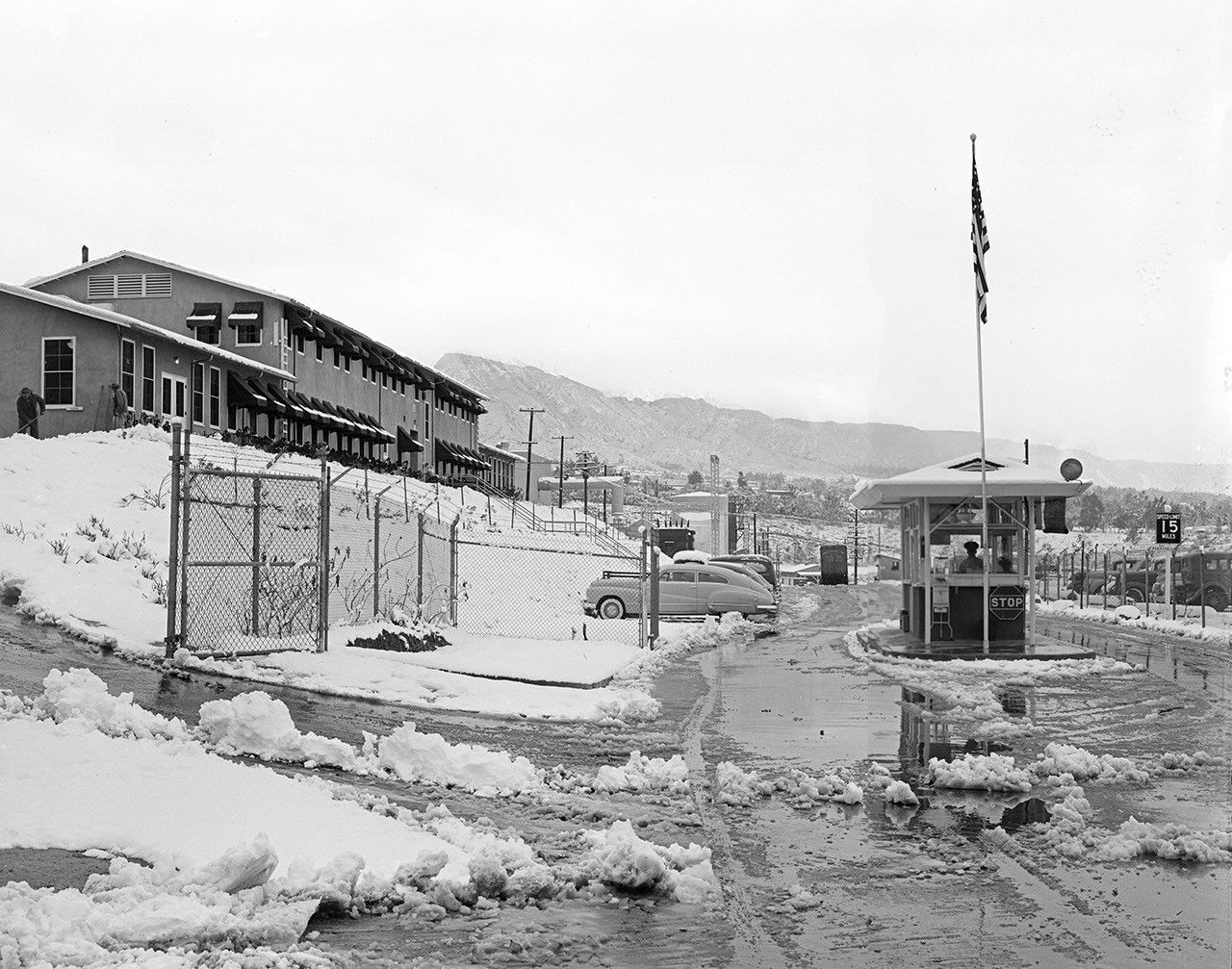 This archival photograph from 1949 shows the main entrance gate to the Jet Propulsion Laboratory in Pasadena, California, after a snowstorm. To the left is JPL's administration building at the time. Building 67 is the Materials Research Building today.