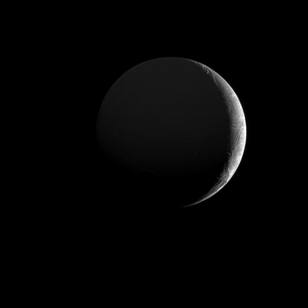The low angle of sunlight along the slim crescent of Saturn's moon Enceladus highlights the many fractures and furrows on its icy surface, as seen by NASA's Cassini spacecraft.