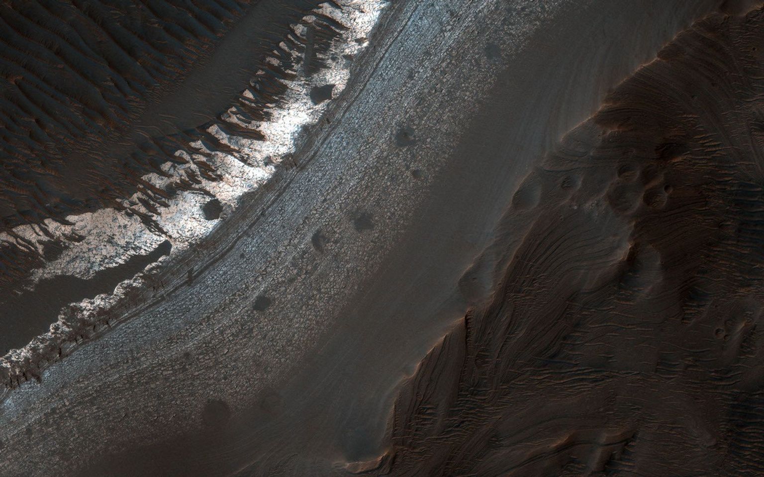 Holden Crater in southern Margaritifer Terra displays a series of finely layered deposits appearing beneath a cap of alluvial fan materials on its floor. This image was captured by NASA's Mars Reconnaissance Orbiter.