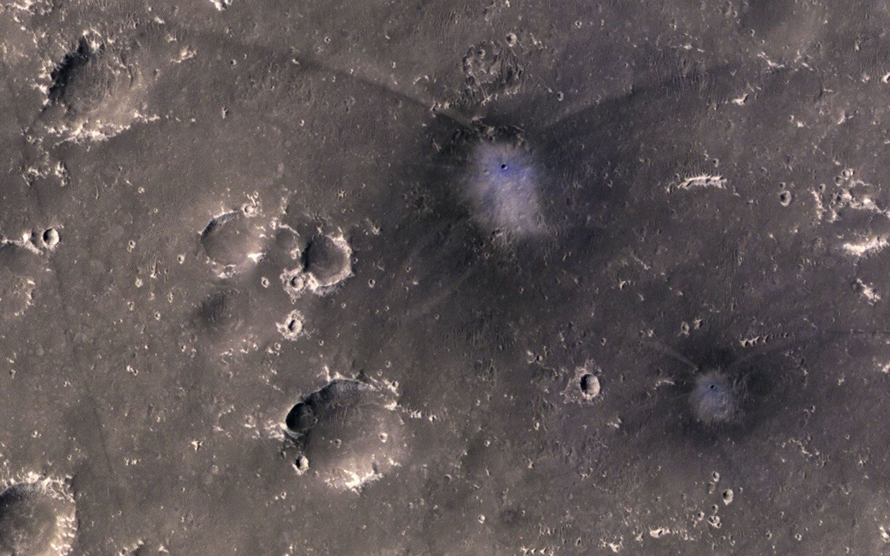 This image from NASA's Mars Reconnaissance Orbiter shows two new craters on Mars with the same distinctive pattern of relatively blue ejecta surrounded by a dark blast zone and arcing patterns. This pattern indicates an oblique impact angle with a bolide.