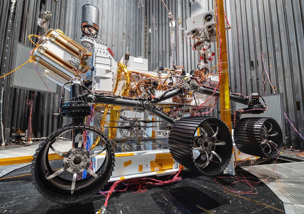 The Ingenuity Mars Helicopter can be seen between the left and center wheels of the Mars 2020 Perseverance rover. The image was taken in the vacuum chamber at JPL on Oct. 1, 2019.