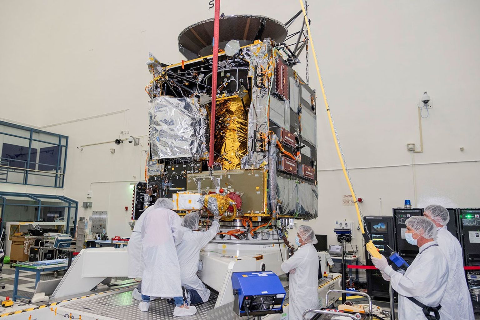 Engineers at NASA's Jet Propulsion Laboratory work to integrate Hall thrusters into the agency's Psyche spacecraft in July 2021. One of the thrusters is visible on the side of the spacecraft underneath a red protective cover.