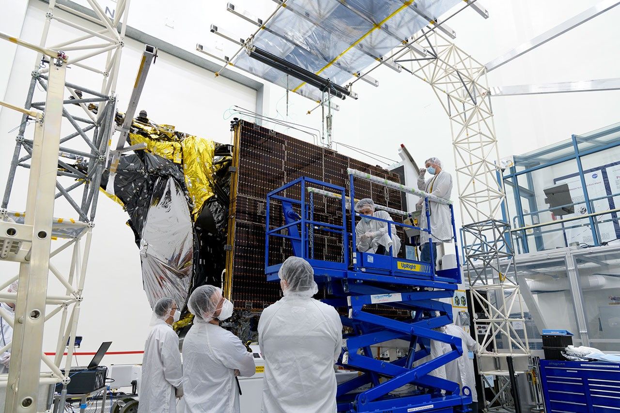 Before a deployment test in a clean room at JPL, engineers examine one of Psyche's two solar arrays. The arrays are folded and stowed flush with the chassis, as shown here, before launch and then deployed in flight.