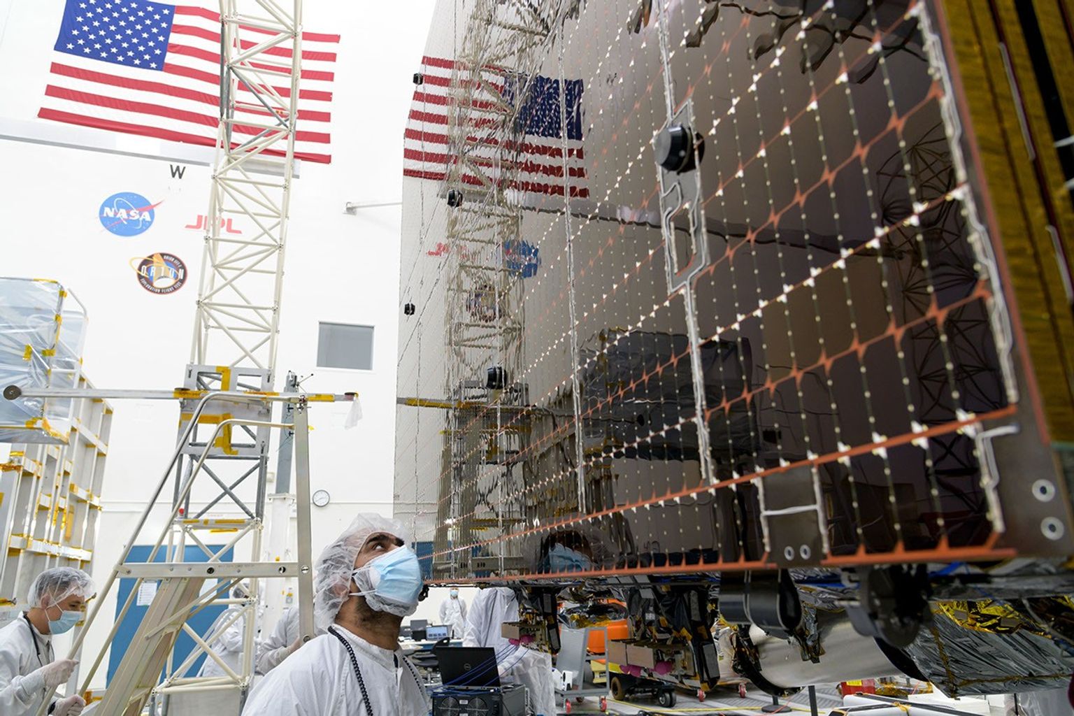 An engineer examines a panel on a stowed solar array on NASA's Psyche spacecraft prior to a deployment test in a clean at JPL. The panels are designed to work in low-light conditions, far from the Sun.