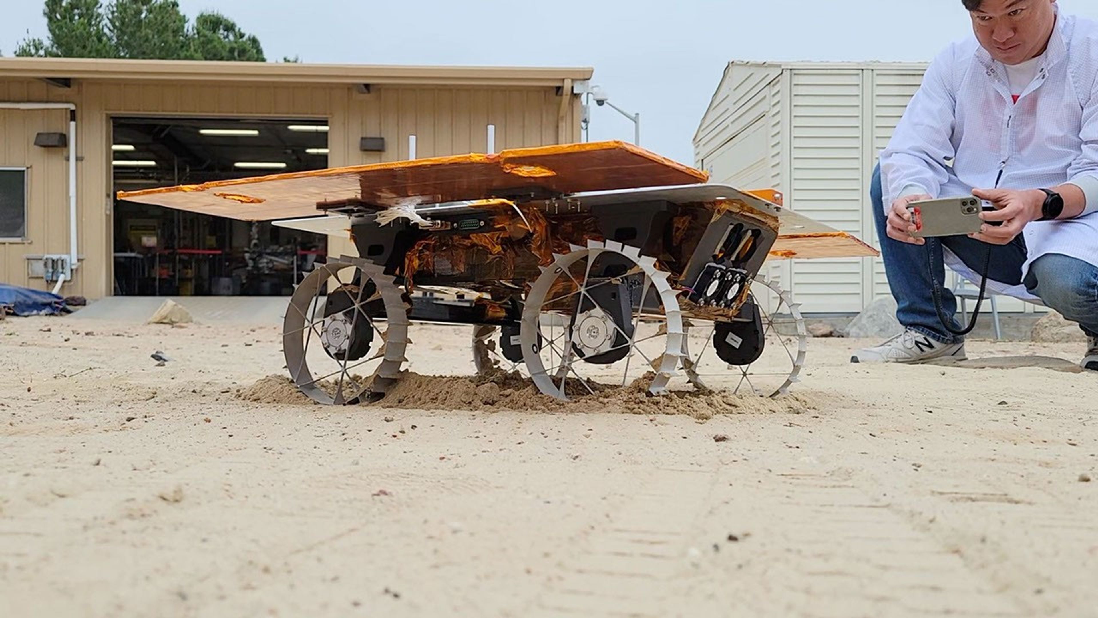Engineer Kristopher Sherrill observes a development model rover during a test for NASA's CADRE technology demonstration in JPL's Mars Yard in June, 2023.