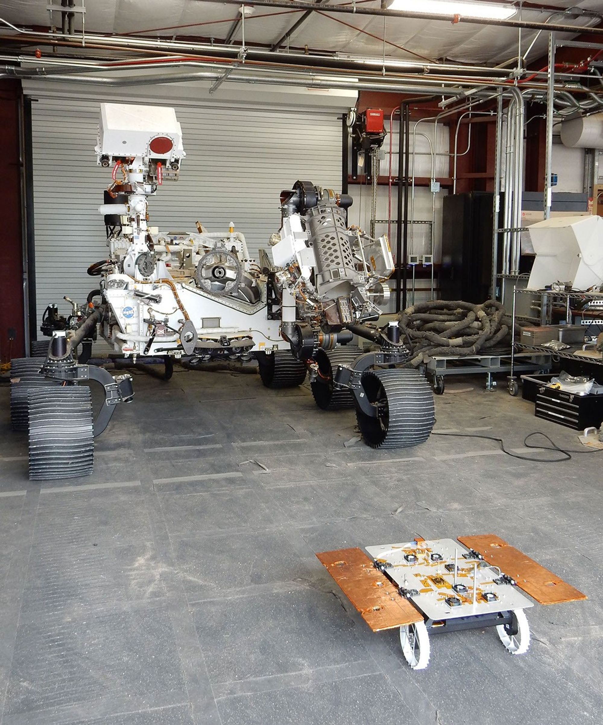 A CADRE test rover appears to catch the attention of the much larger engineering model of NASA's Perseverance rover, called OPTIMISM, at JPL's Mars Yard.