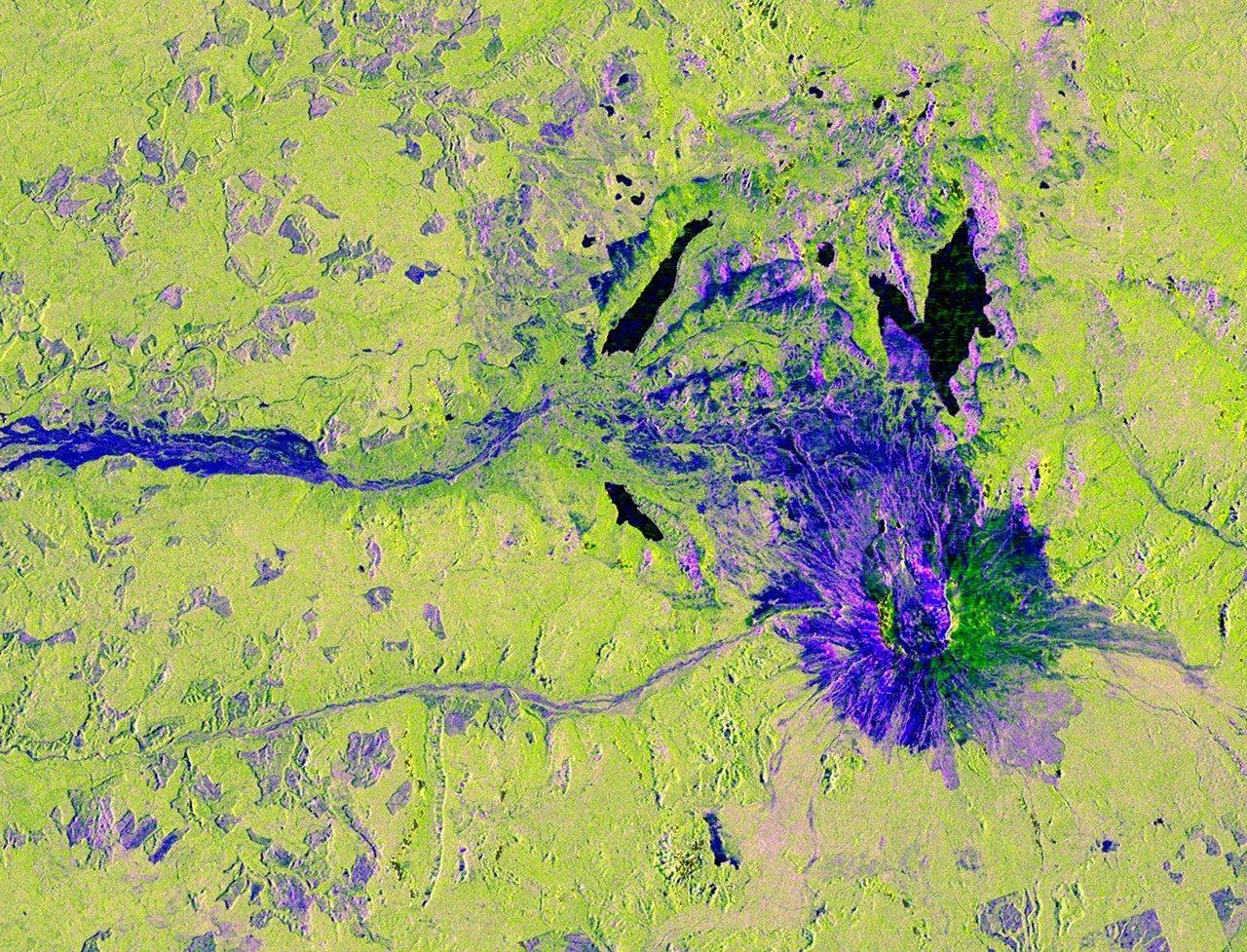 An overhead view of a mountain and the area around it, with unnatural colors added to the radar image. The ground is colored a bright spring green, while the mountain is purple, spreading out like a flower, with a center that's bright fluorescent yellow-green.