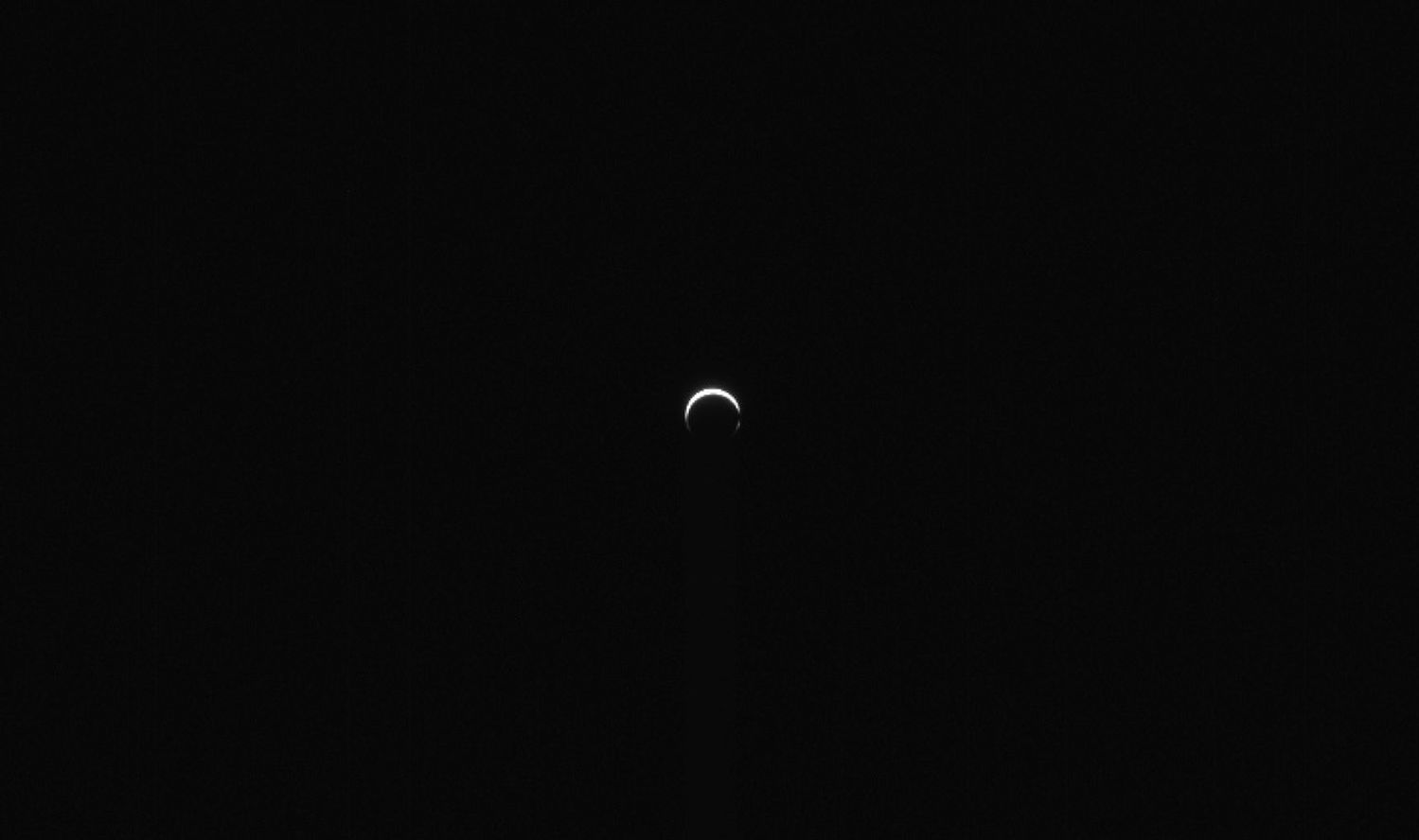 Against a vast black background, a small white crescent shape occupies the center of the image. The crescent is thickest at top and open on the bottom. 