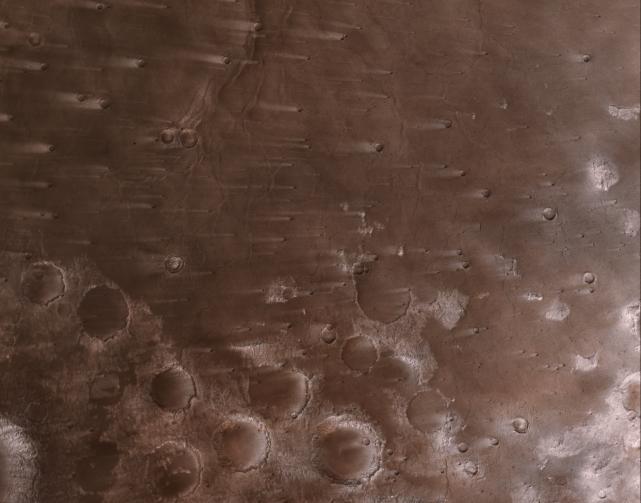 An overhead view of a reddish-brown Martian landscape, heavily pockmarked with impact craters and covered in numerous parallel, wind-blown streaks stretching horizontally across the terrain.