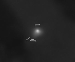 On a largely black background, interstellar comet 3I/ATLAS appears as a white smudge with a semicircular shape at its core. A transparent white cloud extends slightly from the comet toward the bottom left of the image and, to a lesser extent, toward the right side of the image. A scale bar indicates a distance of 932 miles above the comet, and an arrow pointing from the comet to the bottom left of the image is labeled “comet trajectory."