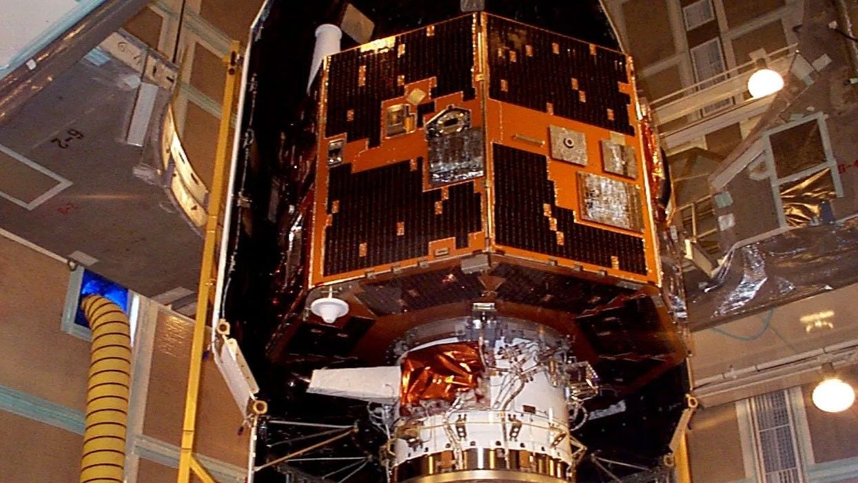 An orange and black spacecraft sits on a work stand.