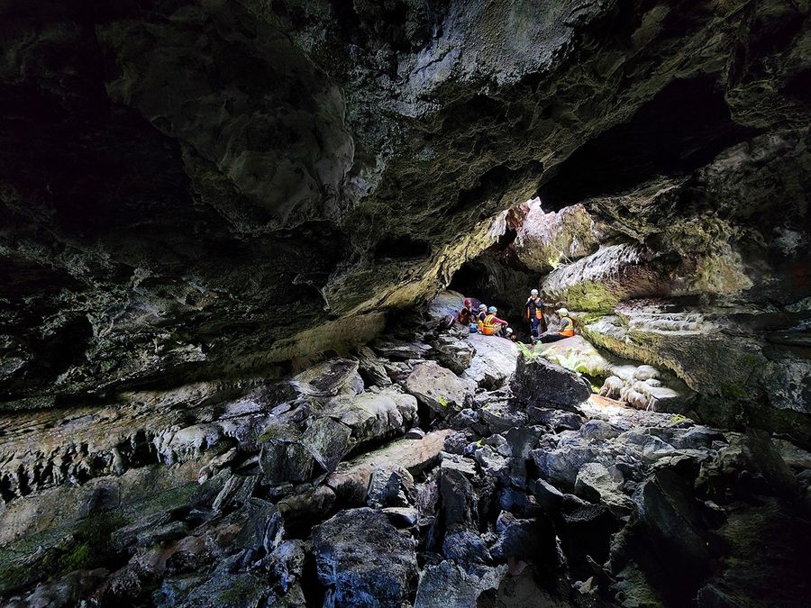 Group of workers wearing high-visibility vests and helmets, sitting under a natural skylight in a rocky cave.