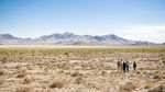 Dry desert plain dotted with low shrubs stretches toward layered mountains.