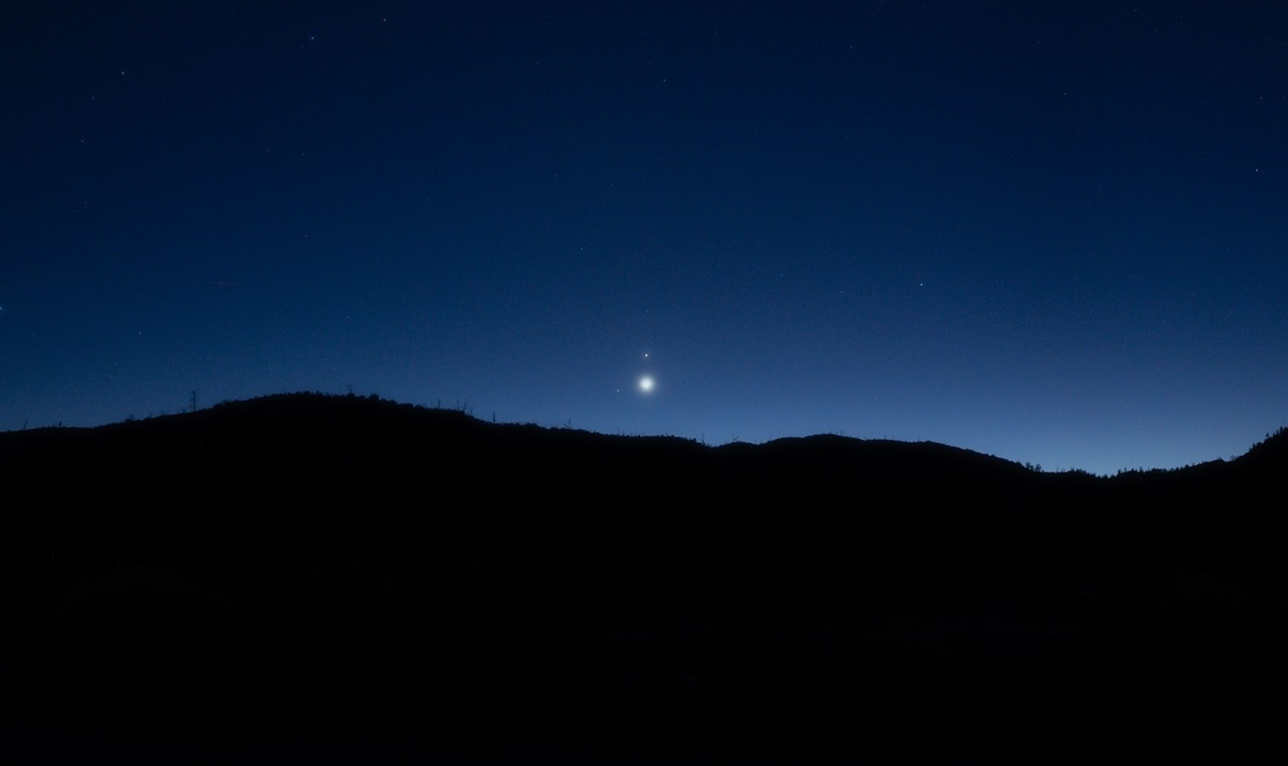 Two bright planets appear close to each other in the night sky as they hover above a hill.