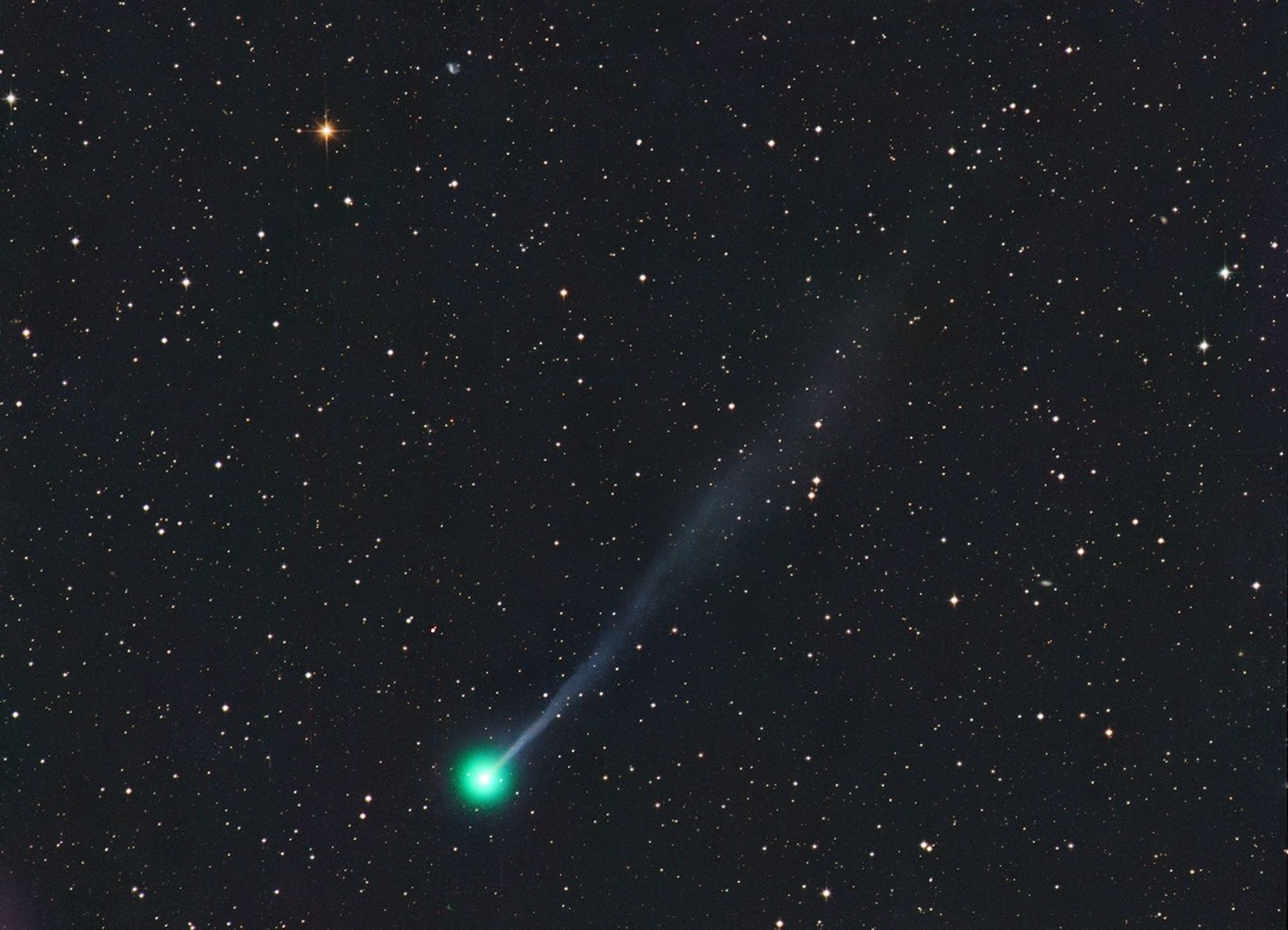 Comet C/2025 R3 glows green with a long blue ion tail stretching across a star-filled sky, previewing its closest approach to Earth on April 27 and potential visibility through binoculars.