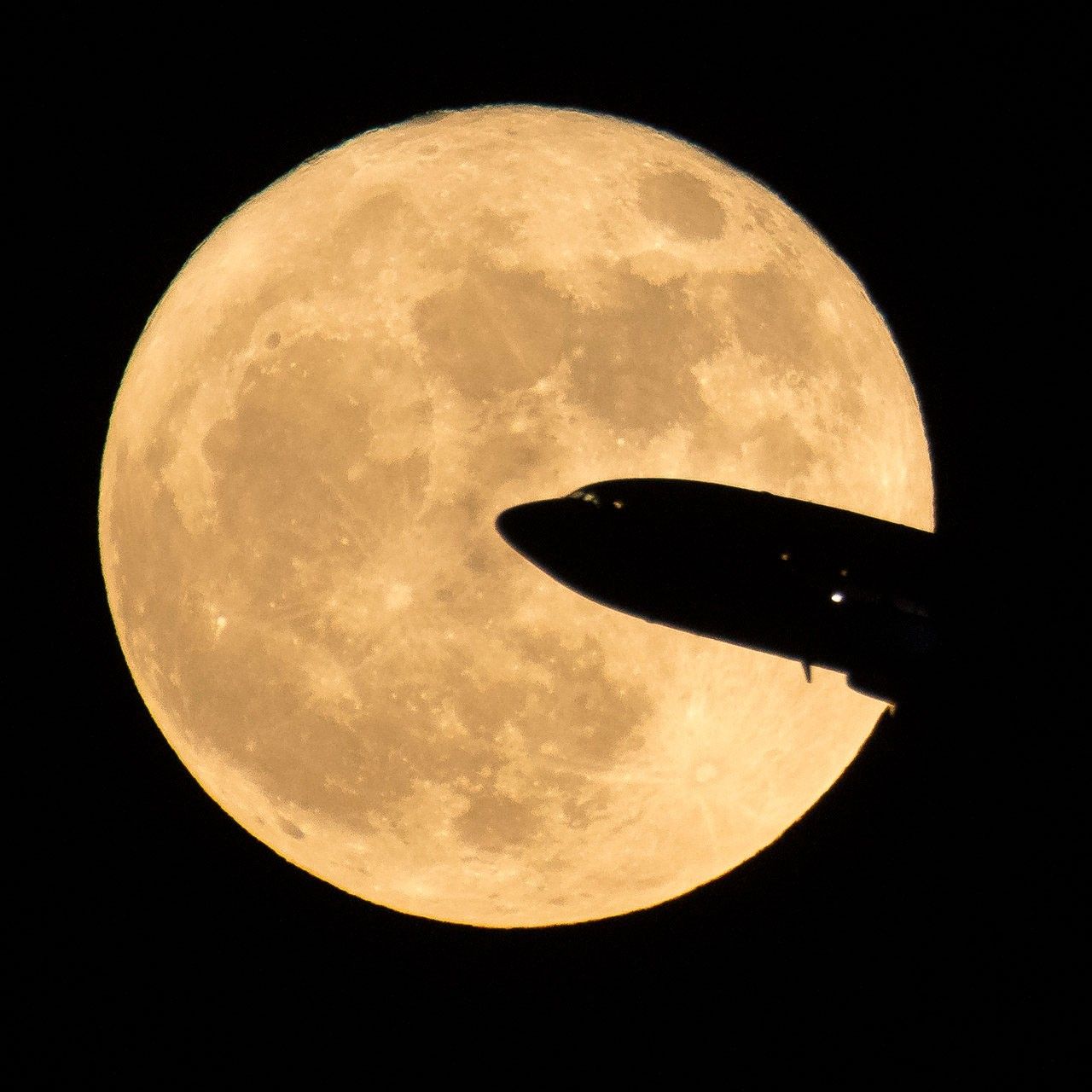 full moon with silhouette of airliner in foreground