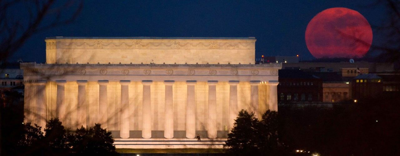 Reddish full moon rising next to Lincoln Memorial.
