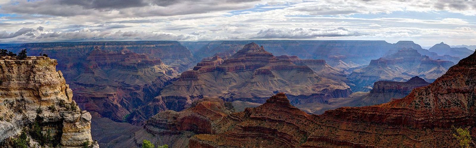 View of sprawling Grand Canyon showing many hues of red rock and against a blue sky.