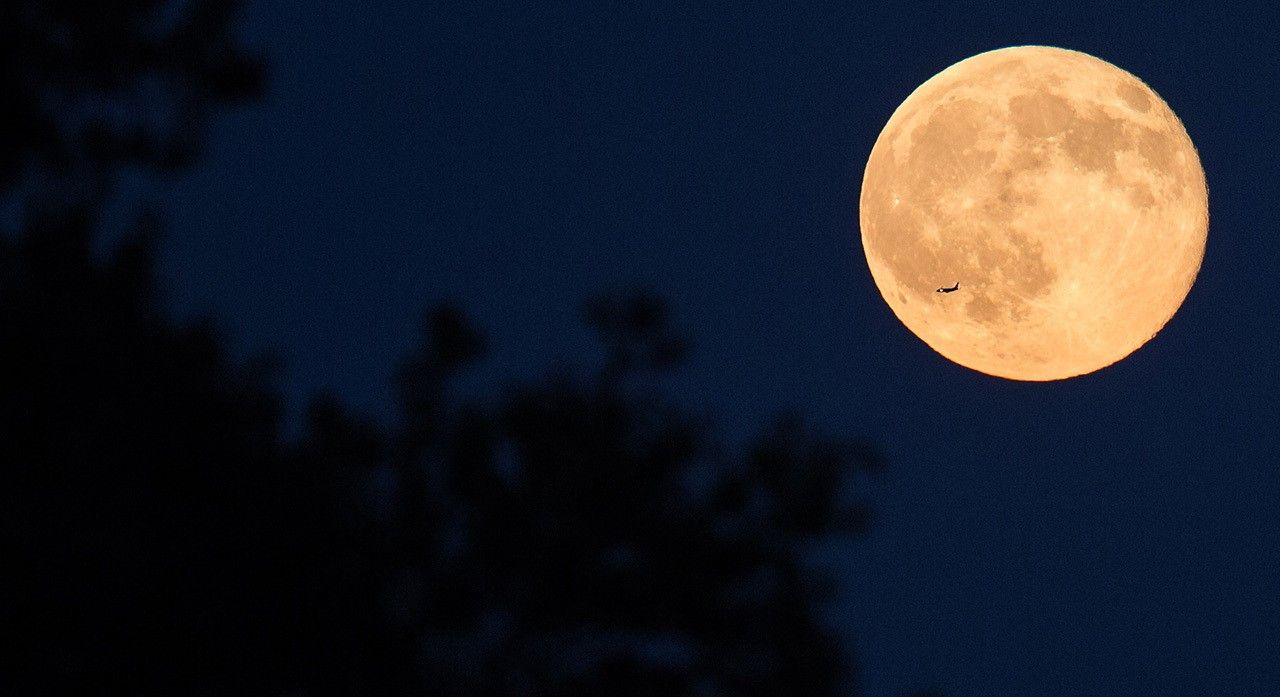 Image of a plane with the full Moon behind it