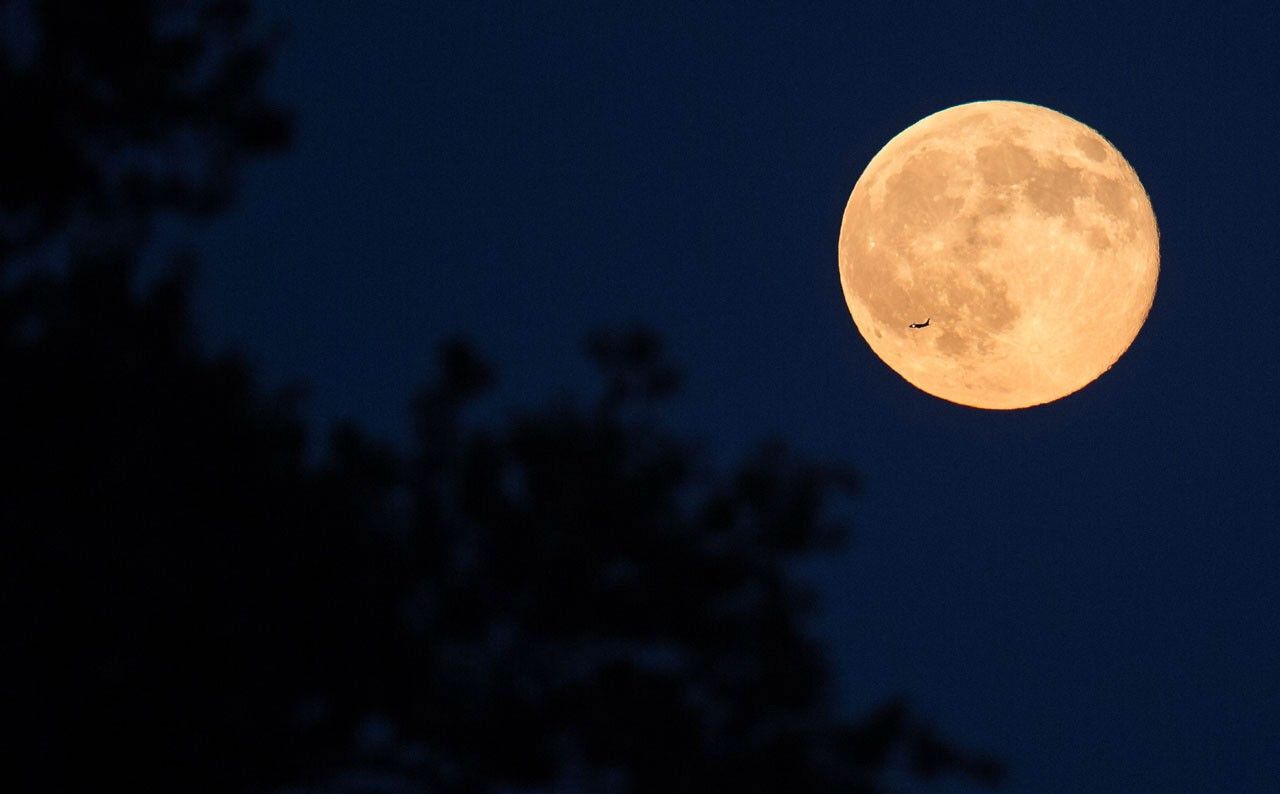 An airliner is silhouetted against a bright full moon on a summer night.