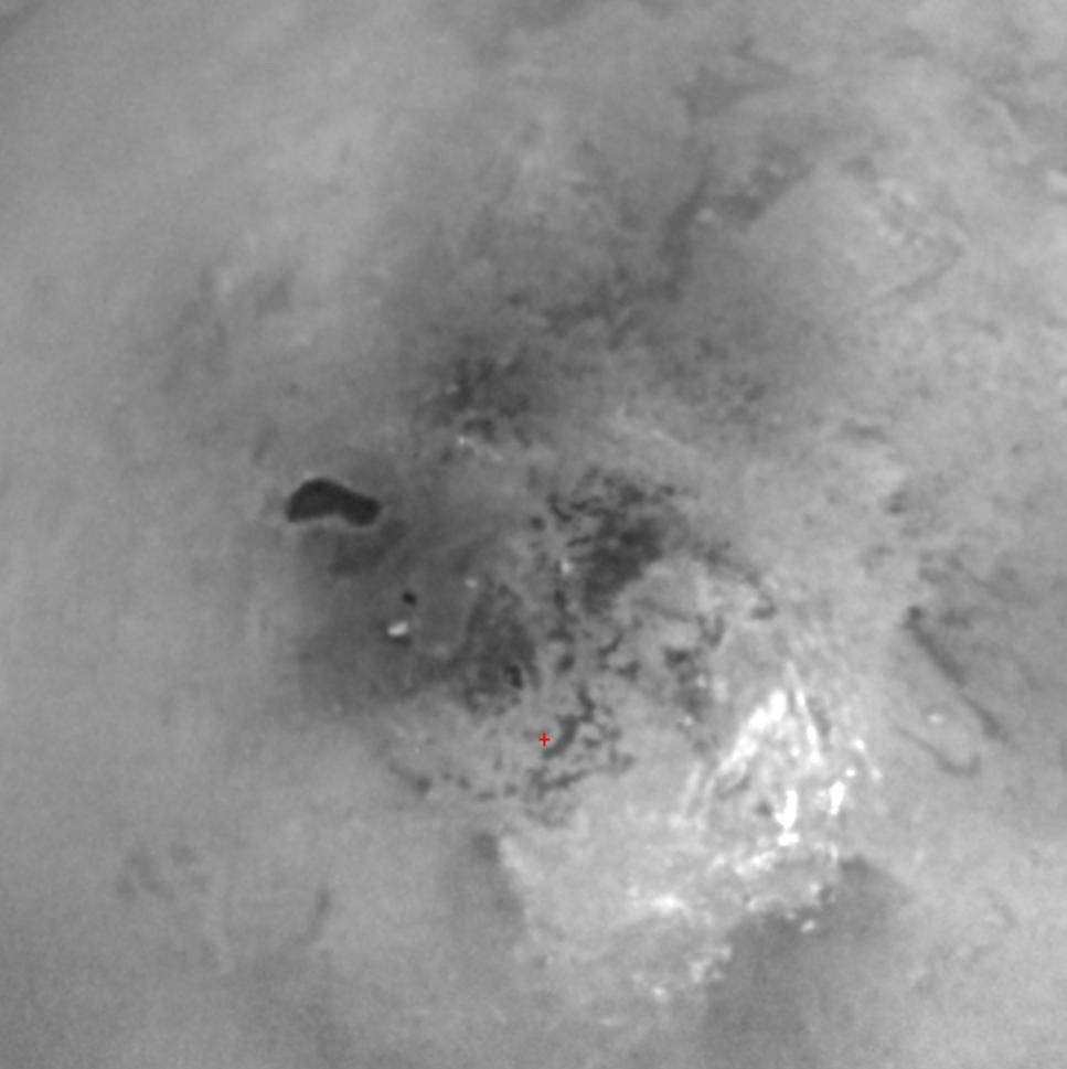 This view of Titan's south pole reveals the intriguing dark feature named Ontario Lacus and a host of smaller features dotting the south polar region. A red cross below the center in the scene marks the pole.