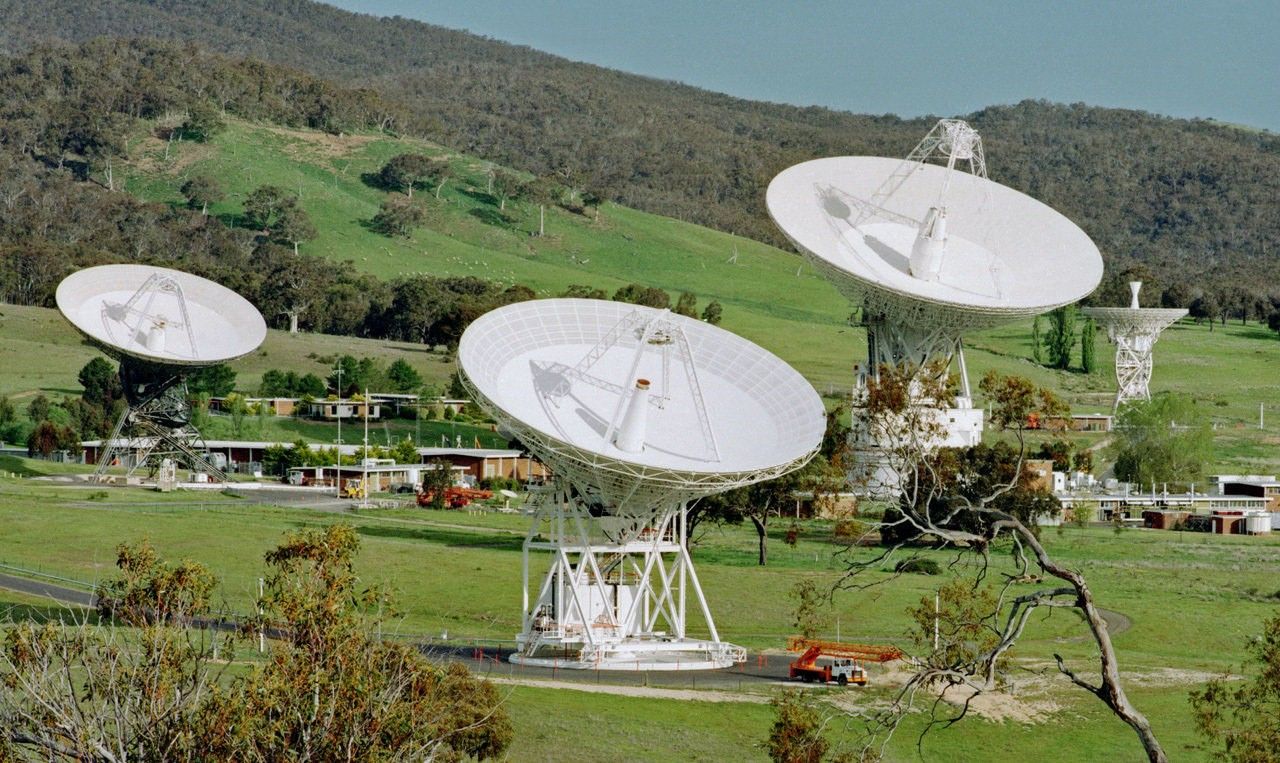 Large, white dish-shaped antennas on a green, grassy field.