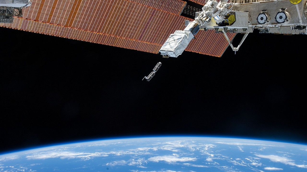 Two small satellites emerging from dispenser on space station.