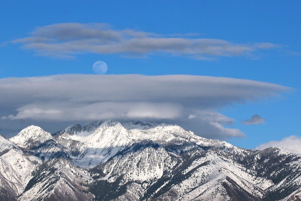 nearly full Moon rising over cloudy mountaintops