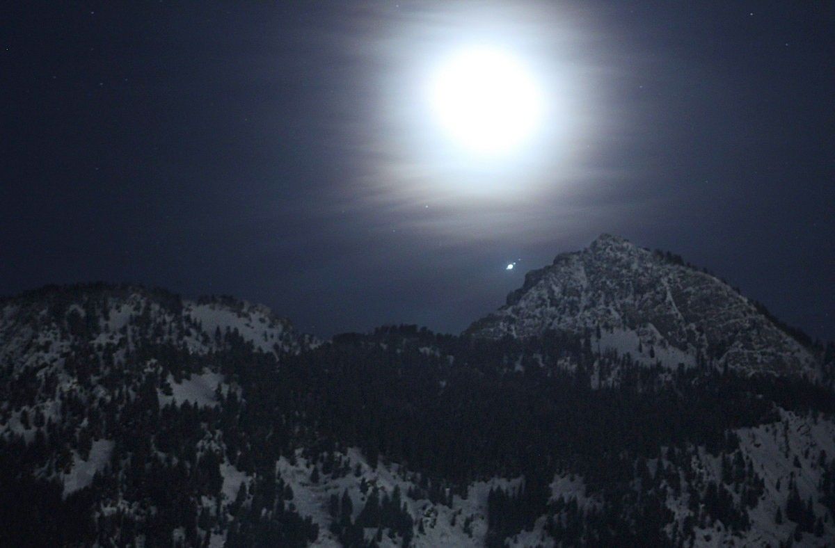 The Moon, lost in haze, rises over the Wasatch Mountains near Salt Lake City in February 2019. The planet Jupiter can be seen nearby, along with three of its moons. Credit: NASA/Bill Dunford  | › Full image and caption