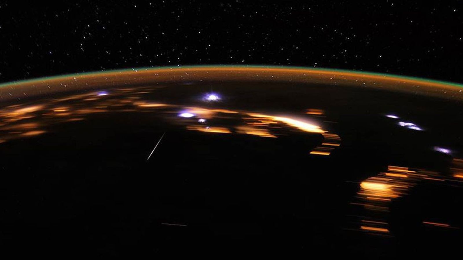 Bright white lights over Earth as meteors collide with the atmosphere. Stars can be seen in the night sky above the curvature of the planet.